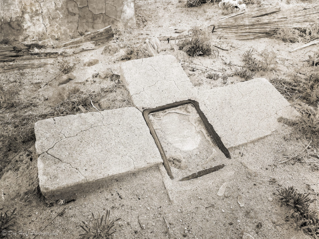 A concrete grave marker is buried in the sand at Our Lady of Guadalupe Cemetery in Peralta, New Mexico.