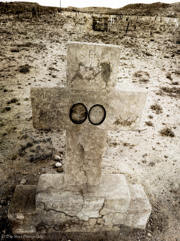 A concrete cross grave marker with eyes at Our Lady of Guadalupe Cemetery in Peralta, New Mexico.